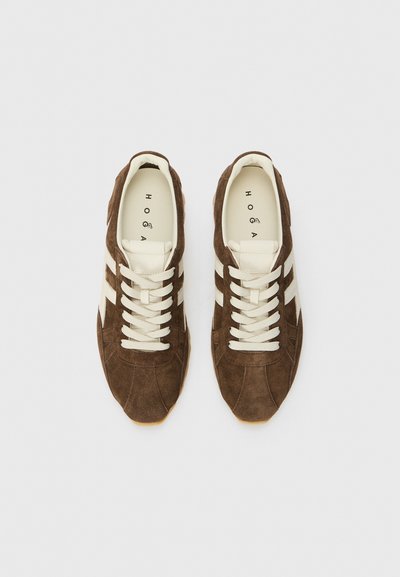 Braune Wildledersneaker mit cremefarbenen Schnürsenkeln und drei cremefarbenen Streifen auf jeder Seite. Gummisohle, runde Zehenform und geprägtes Markenlogo im Inneren.