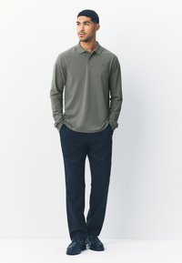 Tricou polo cu mânecă lungă, verde măsliniu, cu guler, asortat cu pantaloni bleumarin și pantofi negri, având un design simplu și curat.