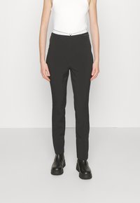Čierne nohavice so slim fit, s hladkou textúrou a pásom s kontrastnou šnúrkou na stiahnutie. Strihované po členky a skombinované s čiernymi topánkami.