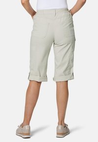 Lichtbeige cargoshorts met opgerolde cuffs, twee achterzakken en een elastische tailleband, gecombineerd met beige schoenen met textuuraccenten.