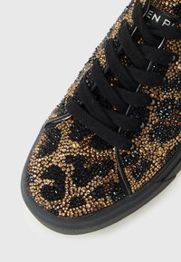 Gros plan sur l'orteil d'une chaussure de sport avec des lacets noirs et des strass dorés et noirs scintillants dans un motif léopard.