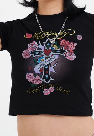 Czarny krótki top z wielokolorowym krzyżem, czerwonym sercem, różowymi różami oraz tekstem „Ed Hardy” i „True to My Love” noszony przez osobę z srebrnym naszyjnikiem.