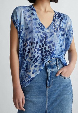 Blå v-hals top med korte ærmer, med leopardmønster i forskellige nuancer af blå og mørk marineblå, lagdelt over et denimskørt.