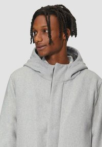 Grijze wollen jas met een grote, zachte capuchon, een ritssluiting aan de voorkant en een minimalistisch ontwerp. Kenmerkt zich door een subtiele textuur en strakke lijnen.