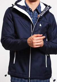 Giacca blu navy con cappuccio foderato bianco, chiusura frontale con cerniera e due tasche laterali. Presenta una texture liscia e dettagli in metallo argentato.