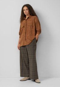 Bruine suède shirt met twee borstzakken, gecombineerd met geruite wijde broek in aardetinten. Zachte textuur en een relaxte pasvorm.