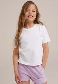 Vit bomull t-shirt med korta ärmar som har en liten präglad blommönster på bröstet, i kombination med ljuslila shorts.