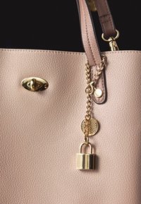 Le sac à main en cuir rose présente une surface texturée, une quincaillerie dorée, une chaîne décorative avec un cadenas et une fermeture ovale.