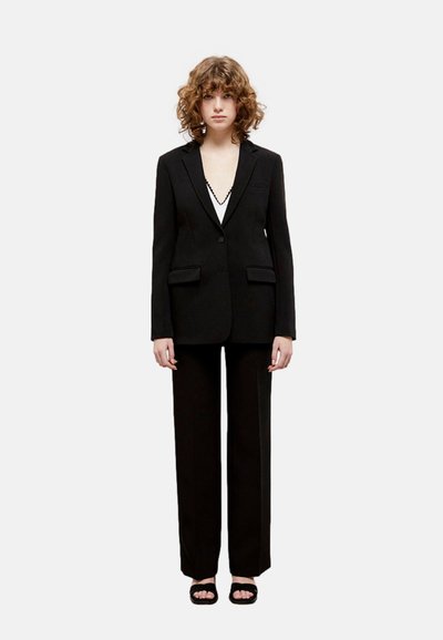 Blazer nero su misura con finitura liscia, due tasche frontali e pantaloni neri coordinati; design minimalista e taglio dritto.