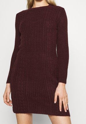 Abito lavorato a maglia in un profondo bordeaux con texture a coste e dettagli a treccia. Maniche lunghe e scollatura rotonda, vestibilità slim, design fino al ginocchio.