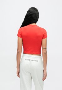 Červené krátke tričko s okrúhlym výstrihom, skrátené rukávy, kombinované so svetlošedými teplákmi s nápisom "NIKE SHOX" na zadnej strane.