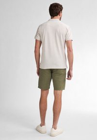 Beige polo shirt with short sleeves, paired with olive green shorts. The outfit is completed with light sneakers, shown from the back.