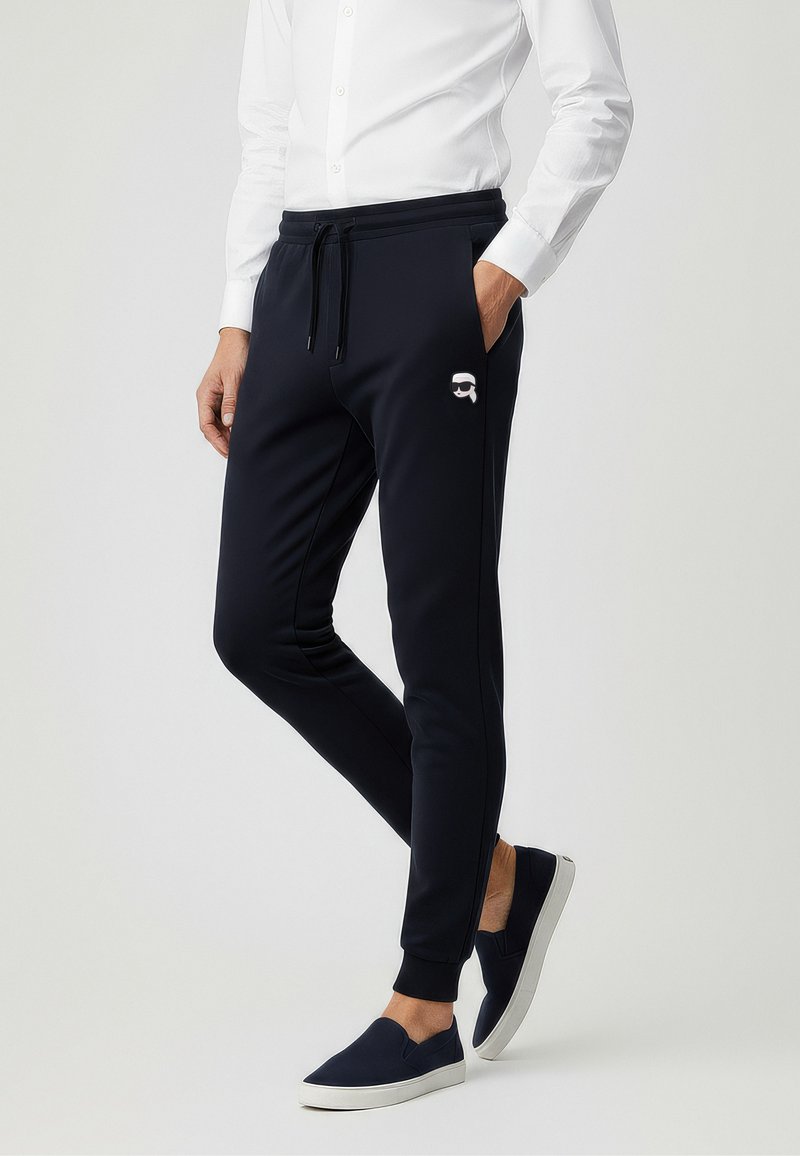 Navyblaue Jogginghosen aus weichem Stoff mit Seitentaschen und elastischen Bündchen. Mit einem weißen Logo auf dem Oberschenkel.