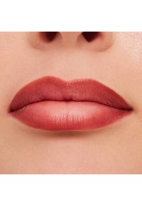 Matowa szminka nałożona na usta z efektem gradientu, o ciepłym koralowym odcieniu i gładkiej teksturze. Otaczająca skóra wydaje się miękka.