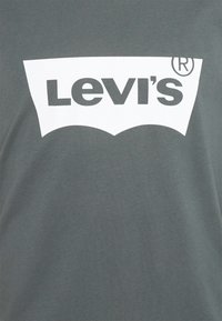 Grå bomullströja med en framträdande vit Levi's-logotyp och en distinkt böjd bakgrundsdesign. Mjuk textur, korta ärmar.