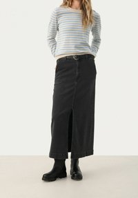 Jupe maxi en denim noir avec une fente devant, présentant une coupe classique et des passants pour ceinture, associée à une chemise à manches longues rayée.