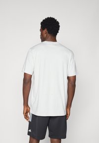 Hvid bomulds t-shirt med korte ærmer og en rund halsudskæring, båret med sorte atletisk shorts med tre hvide striber på siden.