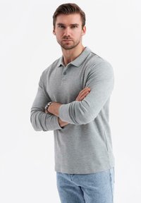 Grå långärmad polo skjorta med krage, med två knappar och avslappnad passform. Bärs med ljusblå jeans. Slät m texture.