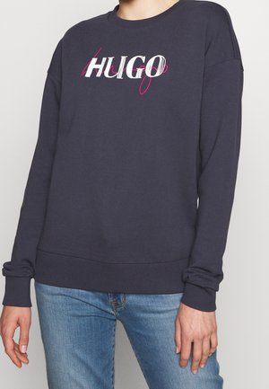 Marineblå sweatshirt med ribbad nederkant och ärmslut, med en vit och rosa "HUGO" grafik på framsidan. Mjuk tyg med en avslappnad passform.