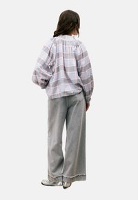 Geruite, lichte blouse met puffmouwen in pastelkleuren, gecombineerd met losse grijze broeken met uitgefranjeerde zomen en zilveren schoenen.