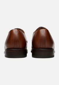 Braune Leder-Dressschuhe mit glatter Oberfläche, runder Spitze und niedrigem Absatz; sie verfügen über dezente Nähte und ein kleines Logodetail auf der Rückseite.