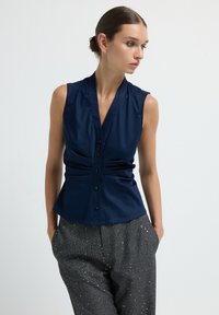 Blusa senza maniche blu navy con scollatura a V e bottoni decorativi, caratterizzata da dettagli arricciati per una silhouette aderente.