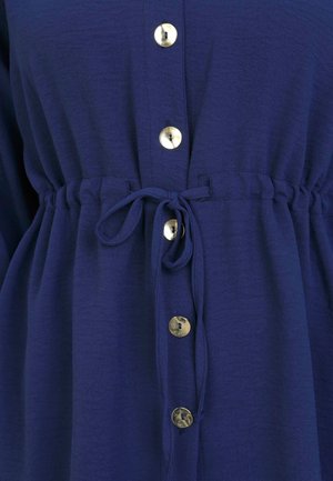 Robe chemise bleu marine avec taille à cordon, dotée de grands boutons dorés et d'un tissu léger texturé.