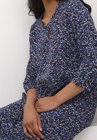 Modré šaty s květinovým vzorem vyrobené z lehké tkaniny. Mají výstřih ve tvaru klíčové dírky a volné rukávy. Texturovaný design s několika barvami.