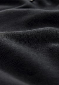 Zwarte stof met een gladde, licht rekbare textuur, die zachte plooien en een consistent weefpatroon vertoont. Geen zichtbare hardware of accenten.