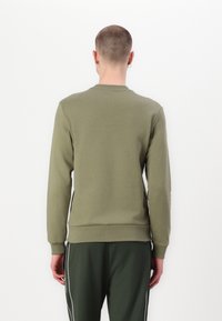 Sudadera verde oliva con mangas largas, cuello redondo y puños de canalé. Fabricada con un tejido suave, presenta un diseño simple y liso.