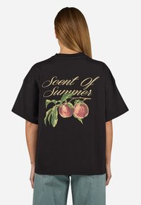 Zwarte oversized t-shirt met een perzikafbeelding met groene bladeren en de tekst "Scent Of Summer" in gouden script op de achterkant.