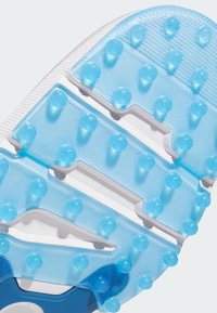 Kenkäpohja, jossa on läpikuultava sininen muotoilu, jossa on teksturoidut pitoalueet ja pyöreät nastat, valkoisen pohjan ja vahvistetun sinisen korosteen päällä.