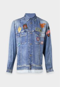 Veste en jean bleue avec fermeture à boutons, poches poitrine et plusieurs écussons brodés colorés à l'avant et sur les manches.