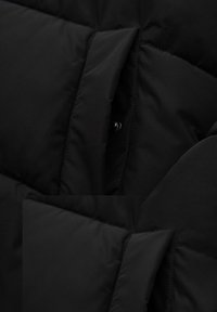 Sort polstret jakke med quiltet design, struktureret stof og knapper på det indre for; glat overflade uden synlige mønstre.