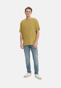 Camiseta de algodón verde oliva con un corte relajado, mangas cortas, cuello redondo, combinada con jeans de denim azul claro y zapatillas blancas.