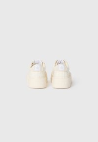 Et par off-white plattform sneakers vist fra baksiden med stjernelogo på hæltappen og tykke gummisåler på ensfarget bakgrunn.
