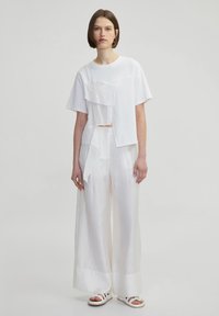 White cropped t-shirt with layered fabric texture, paired with wide-leg white pants in a lightweight fabric, and white strappy sandals.