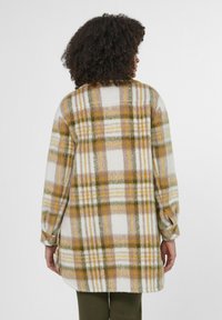 Geruite flanellen blouse in beige, geel en groen met een zachte textuur. Voorzien van lange mouwen en een gebogen zoom. Zichtbare knoopdetails op de manchetten.