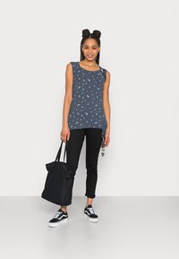 Top sem mangas azul-marinho com um padrão floral, combinado com calças pretas ajustadas e uma bolsa tote preta. Modelo usando sapatilhas pretas e brancas.