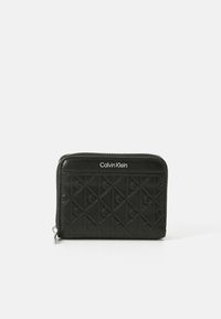Ce portefeuille zippé noir présente un motif en diamant embossé et un logo Calvin Klein sur le devant. Fabriqué en matériau lisse. Forme compacte et rectangulaire.