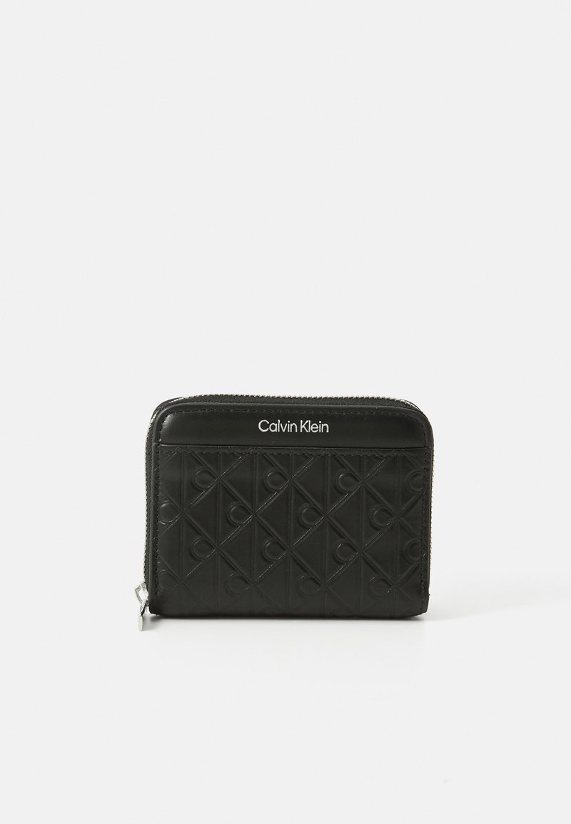 Ce portefeuille zippé noir présente un motif en diamant embossé et un logo Calvin Klein sur le devant. Fabriqué en matériau lisse. Forme compacte et rectangulaire.