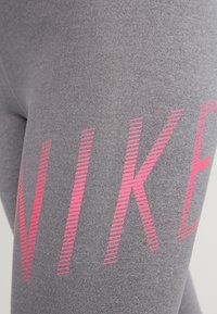 Graue Leggings mit auffälligen, diagonalen pinkfarbenen Streifen und dem Schriftzug "NIKE." Hergestellt aus einem glatten, dehnbaren Stoff für Komfort.