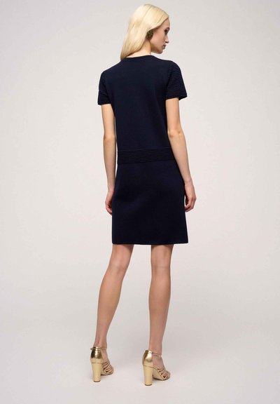 Abito in maglia navy con maniche corte a coste, caratterizzato da una texture orizzontale lungo la vita. Completato con sandali con tacco dorati.