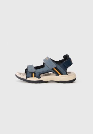 Blue and navy sandal with adjustable Velcro straps, contrasting orange accent, open toe design, and thick beige sole with textured grip.