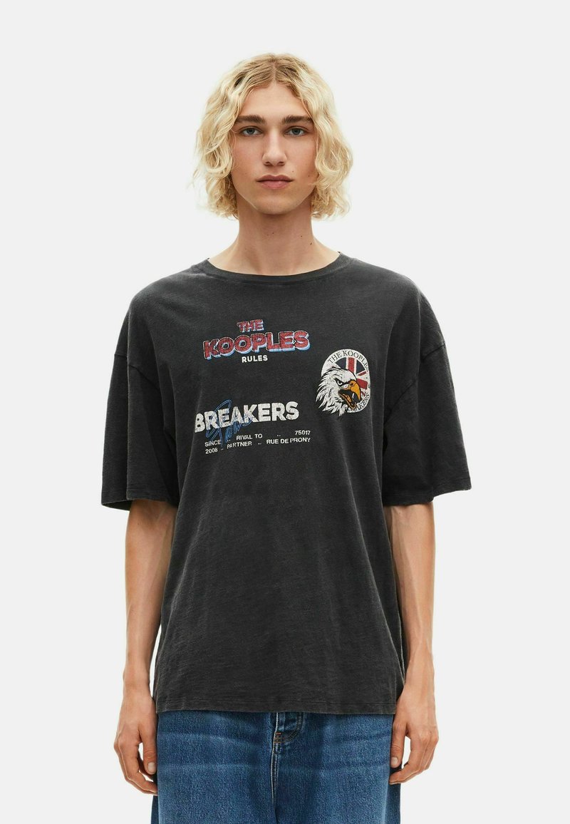 Juodas medvilnės marškinėliai su trumpomis rankovėmis, apykakle, su grafikos atspaudais ir tekstu, įskaitant erelio dizainą ir prekės ženklo logotipą.