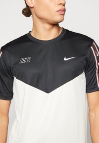 Camisa deportiva de Nike con un diseño negro en la parte superior y blanco en la parte inferior, de mangas cortas, con acentos del logo en el pecho y las mangas.