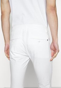 Witte katoenen broek met een smalle pasvorm, voorzien van achterzakken, subtiele stikseldetails en een gladde textuur.