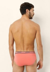 Korallfärgade herrunderkläder i shortsmodell med en midjeresår som har svarta detaljer och varumärkesnamnet. Slät textur, figurnära design och enfärgad.