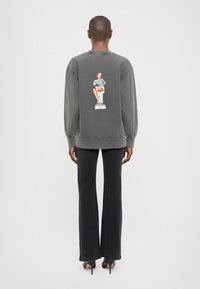 Sudadera gris de gran tamaño con mangas largas, que presenta una impresión gráfica de una figura sentada en la parte posterior. Combinada con pantalones negros de campana.