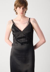 Schwarzes Satin-Nightdress mit V-Ausschnitt, zarter Spitze an den Trägern und einer taillierten Silhouette mit glatter Textur.
